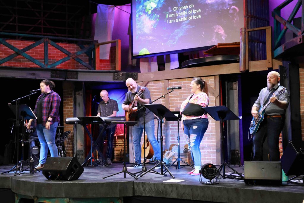 A group of people stand on a stage playing instruments and singing