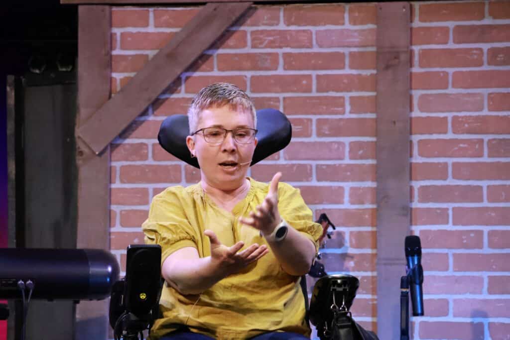 A woman sits in a wheelchair talking and gesturing with her hands